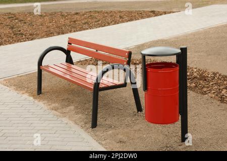 Poubelle en métal rouge près d'un banc en bois dans le parc de la ville Banque D'Images