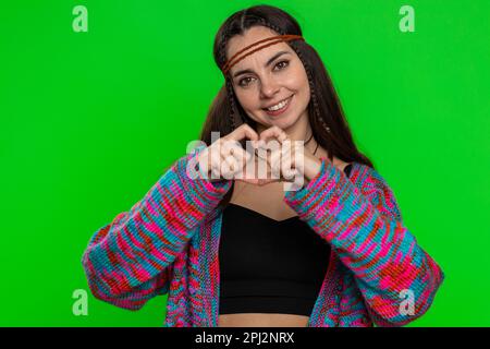 Femme amoureuse. Sourire hippie femme 25 ans fait coeur geste démontre signe d'amour exprime de bons sentiments et de la sympathie. Jolie jeune fille isolée sur fond de chroma clé, écran vert Banque D'Images