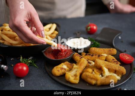 Une femme plonge les frites dans une sauce trempée avec des bâtonnets de mozzarella frits au fromage sur une table Banque D'Images