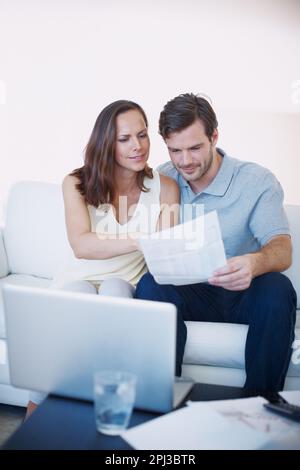 Faire leurs finances personnelles ensemble. Un jeune couple discutant des finances de sa maison tout en étant assis ensemble dans leur salon. Banque D'Images