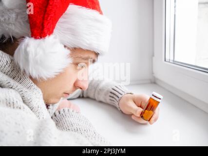 Jeune homme dans le chapeau de Santa tenir une pilule près de la fenêtre dans la salle Banque D'Images