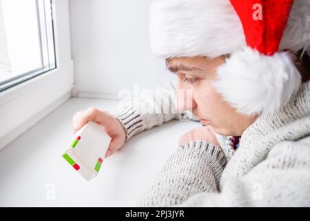 Jeune homme dans le chapeau de Santa tenir une pilule près de la fenêtre dans la salle Banque D'Images
