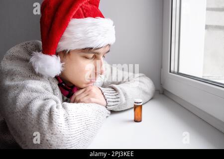 Jeune homme à Santa Hat avec un pillule près de la fenêtre dans la chambre Banque D'Images