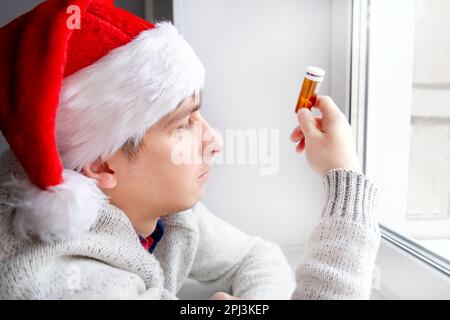 Jeune homme à Santa Hat avec un pillule près de la fenêtre dans la chambre Banque D'Images