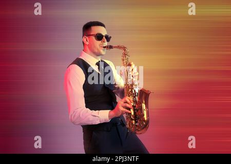 Jeune homme avec une tenue élégante jouant du saxophone sur fond de couleur Banque D'Images
