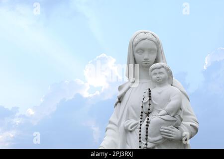 Belle statue de la Vierge Marie et du bébé Jésus avec des perles rosaires en plein air. Espace pour le texte Banque D'Images
