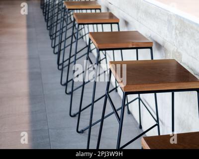 Rangée de chaises de tabouret de bar en bois à côté de comptoir en béton, intérieur de café de style loft. Sièges en bois vides avec décoration de barre en acier noir sur flo en béton Banque D'Images