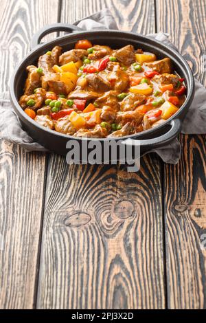 Ragoût de boeuf avec des pommes de terre, des carottes, des pois verts et des épices dans une poêle sur une table en bois. Verticale Banque D'Images