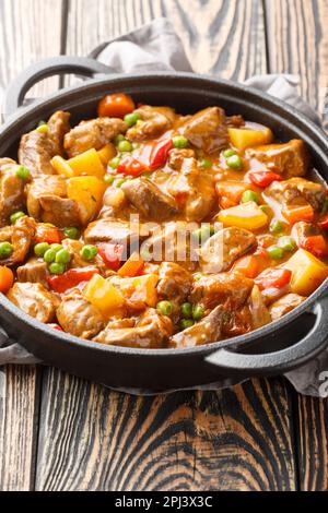 Ragoût de veau avec légumes pommes de terre, carottes, pois verts, oignons et épices gros plan dans une poêle sur une table en bois. Verticale Banque D'Images