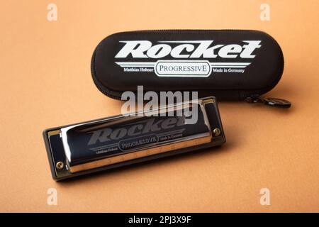 Un professionnel Hohner Rocket diatonique harmonica à côté de son boîtier noir fermé. Sur fond marron clair Banque D'Images