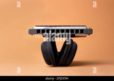 Une harmonica professionnelle repose sur un boîtier noir ouvert, avec des trous dans le cadre. Sur fond marron clair Banque D'Images