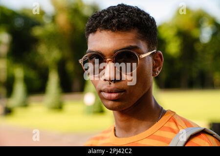 Jeune homme de brunette noir portant des perce et des lunettes de soleil marchant dans le parc Banque D'Images