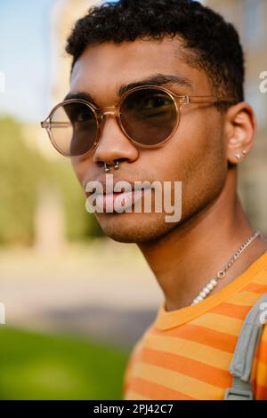 Jeune homme de brunette noir portant des perce et des lunettes de soleil marchant dans le parc Banque D'Images