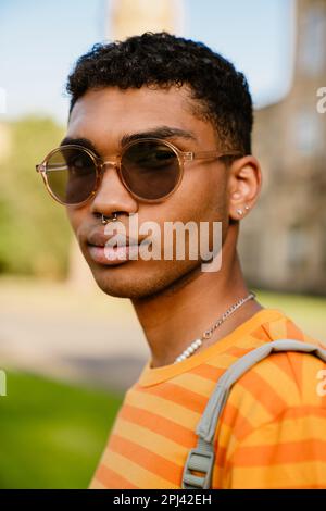 Jeune homme de brunette noir portant des perce et des lunettes de soleil marchant dans le parc Banque D'Images