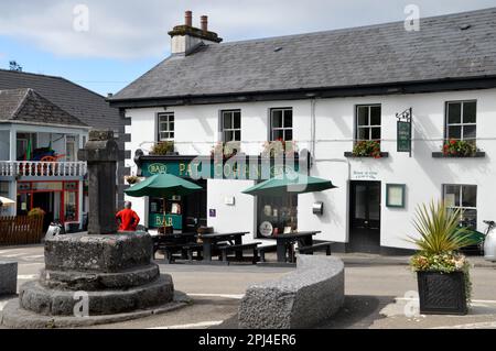 Irlande, Comté de Mayo, Cong : croix de pierre et pub picuresque sur la place du village. Banque D'Images