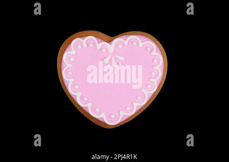 biscuits au gingembre faits maison en forme de coeur avec glaçure rose isolée sur un fond noir vue de dessus avec masque Banque D'Images