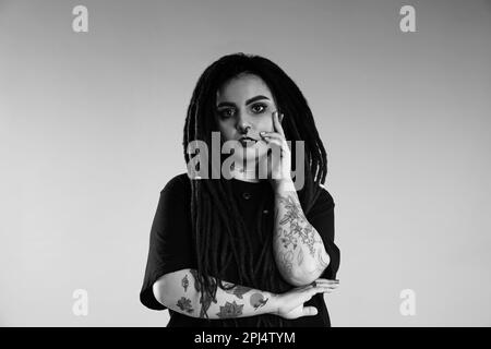 Belle jeune femme avec tatouages sur fond clair. Photographie en noir et blanc Banque D'Images