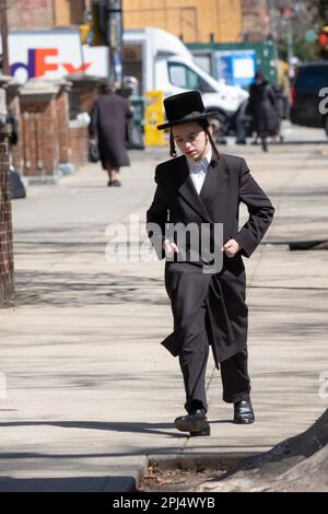 Un adolescent juif hassidique marchant avec ses mains dans ses poches lors d'une journée froide au début du printemps. À New York. Banque D'Images