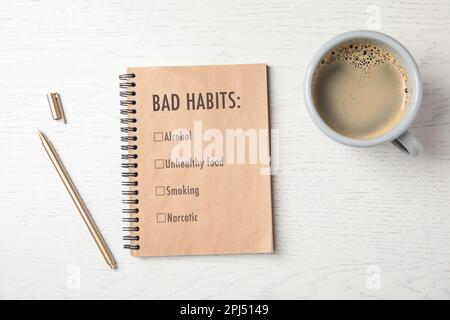 Carnet avec liste de mauvaises habitudes, stylo et tasse de café sur table en bois blanc, plat. Changez votre style de vie Banque D'Images