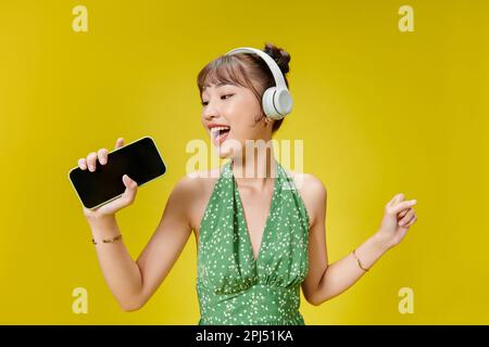 Photo d'une adorable femme tendance en été en train d'écouter de la musique via un casque sans fil et de tenir un téléphone portable Banque D'Images