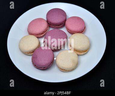 Macarons dans une assiette blanche sur fond noir. Biscuits sucrés colorés. Banque D'Images