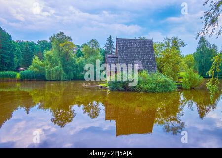 La petite maison de chasseur en bois se reflète sur la surface miroir transparente du lac forestier, situé dans la ferme de chasse de Styr, village de Zbrui, Lviv Banque D'Images