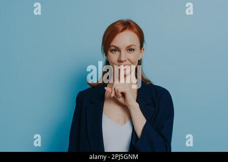 Taisez-vous. Jeune femme à cheveux rouges demandant de garder le silence ou de ne pas le dire secret, femme d'affaires caucasienne tenant le doigt sur les lèvres et faisant LE signe SHHH, dre Banque D'Images