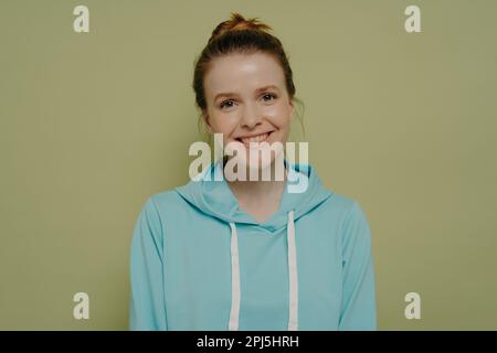 Jolie femme adolescente souriante vêtue d'un pull à capuche de style urbain avec un petit pain qui exprime des émotions positives tout en posant en studio, jeune positif Banque D'Images