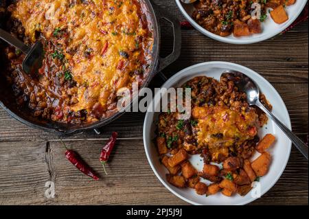 Ragoût de haricots avec fromage cheddar, garniture au piment et patates douces grillées sur une table en bois Banque D'Images