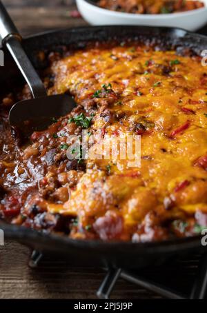 Ragoût de haricots alla Chili con carne avec garniture au fromage cheddar dans une casserole en fonte Banque D'Images