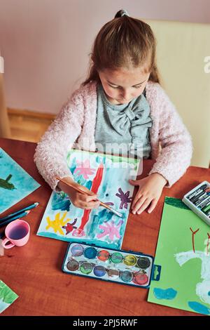 Petite fille de pré-chooler peignant une image en utilisant des peintures colorées et des crayons. Enfant s'amusant à prendre une photo pendant un cours d'art en classe Banque D'Images