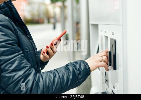 Femme achetant un billet à la machine à billets payant à l'aide de l'application de paiement mobile sur smartphone. Une femme achète un billet de transport public dans un distributeur automatique. PE Banque D'Images