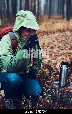 Femme avec sac à dos ayant une pause pendant le voyage d'automne buvant une boisson chaude de thermos fiole le jour d'automne froid. Femme active d'âge moyen errant arou Banque D'Images