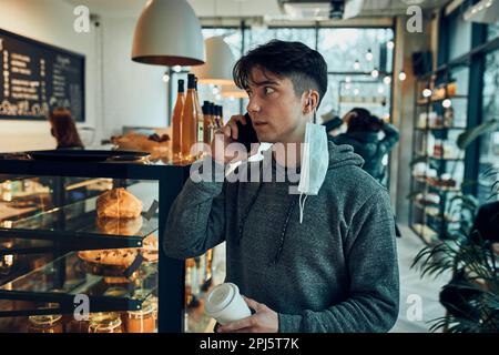 Jeune homme parlant au téléphone au café, ayant un appel important, répondant à un appel, discutant par téléphone portable avec un collègue tout en passant du temps Banque D'Images
