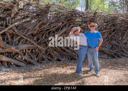 Couple touristique hollandais souriant contre une clôture faite de branches d'arbres et de poteaux en bois dans le parc public, femme penchée tenant son chapeau, bleu vêtements décontractés, Banque D'Images