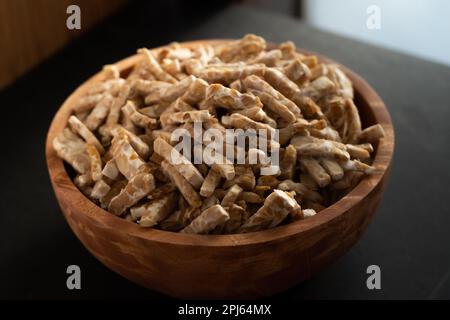 Tempe est un aliment indonésien traditionnel à base de soja fermenté. tranché ​​tempeh dans un bol en bois. Vue rapprochée, arrière-plan en bois sombre. Banque D'Images