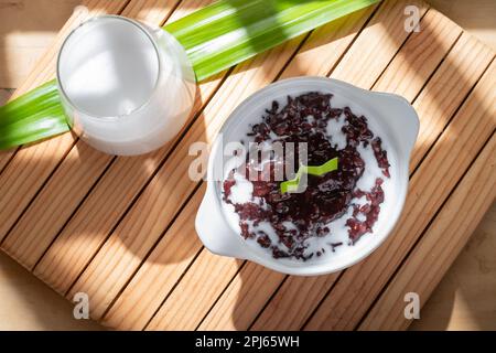 Porridge de riz noir collant avec sauce au lait de coco servi dans un bol blanc. Dessert traditionnel indonésien Banque D'Images