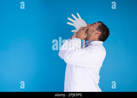 Femme médecin gonflant un gant chirurgical sur un fond bleu isolé. concept de médecine drôle Banque D'Images