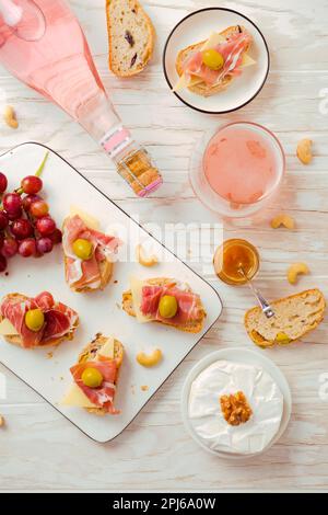 Plats de hors-d'œuvre et sandwichs ouverts avec antipasti italiens, camembert, jambon de Parme et vin de rose sur une table en bois Banque D'Images