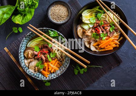 Soupe asiatique de ramen avec nouilles udon, bœuf, shiitake, chou pak choi et carottes sur fond noir Banque D'Images