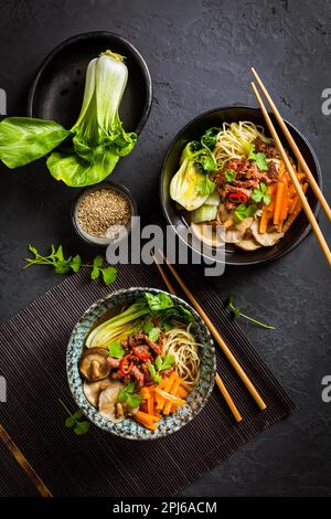 Soupe asiatique de ramen avec nouilles udon, bœuf, shiitake, chou pak choi et carottes sur fond noir Banque D'Images