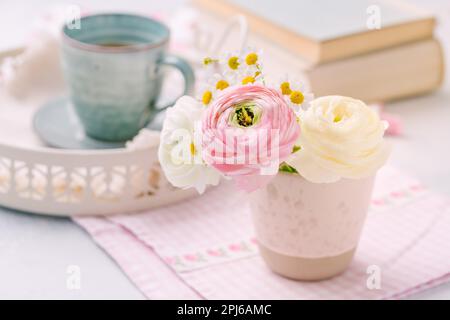 Belle fleur tendre de bouquet frais coupé avec une tasse de livres de thé en arrière-plan sur la table de cuisine Banque D'Images