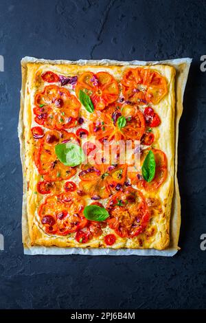 Tarte végétarienne aux tomates ou pizza soufflée aux herbes sur le noir arrière-plan Banque D'Images