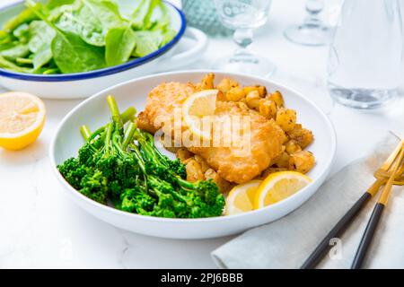 Filet de poisson pané avec pommes de terre cuites au four épicées et salade de brocoli (bimi) avec citron Banque D'Images