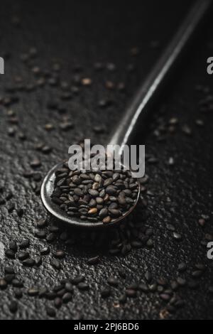 Graines de sésame noir dans une petite cuillère sur fond noir. Prise de vue en studio macro Banque D'Images