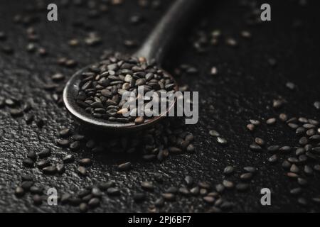 Graines de sésame noir dans une petite cuillère sur fond noir. Prise de vue en studio macro Banque D'Images