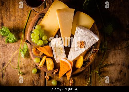Plateau de fromages, assortiment de différents fromages avec verre de vin rouge, raisins sur table en bois Banque D'Images