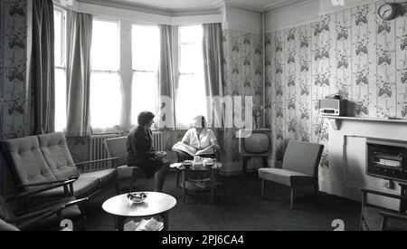 1950s, historique, femme responsable de maison assis avec une femme membre du personnel de cuisine dans un salon à l'auberge de Littlemore, un centre de santé mentale à l'hôpital Littlemore, Oxfordshire, Angleterre, Royaume-Uni. Banque D'Images