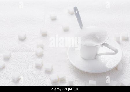 Sucre blanc granulé dans une tasse blanche avec cuillère sur fond blanc Banque D'Images