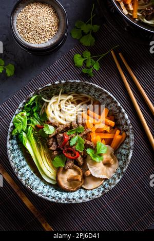 Soupe asiatique de ramen avec nouilles udon, bœuf, shiitake, chou pak choi et carottes sur fond noir Banque D'Images